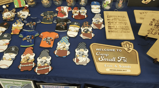 Close-up of playful sports-themed gnome ornaments and engraved camping rules plaques on rich blue fabric; crisp indoor lighting accentuates colors and wood grain.